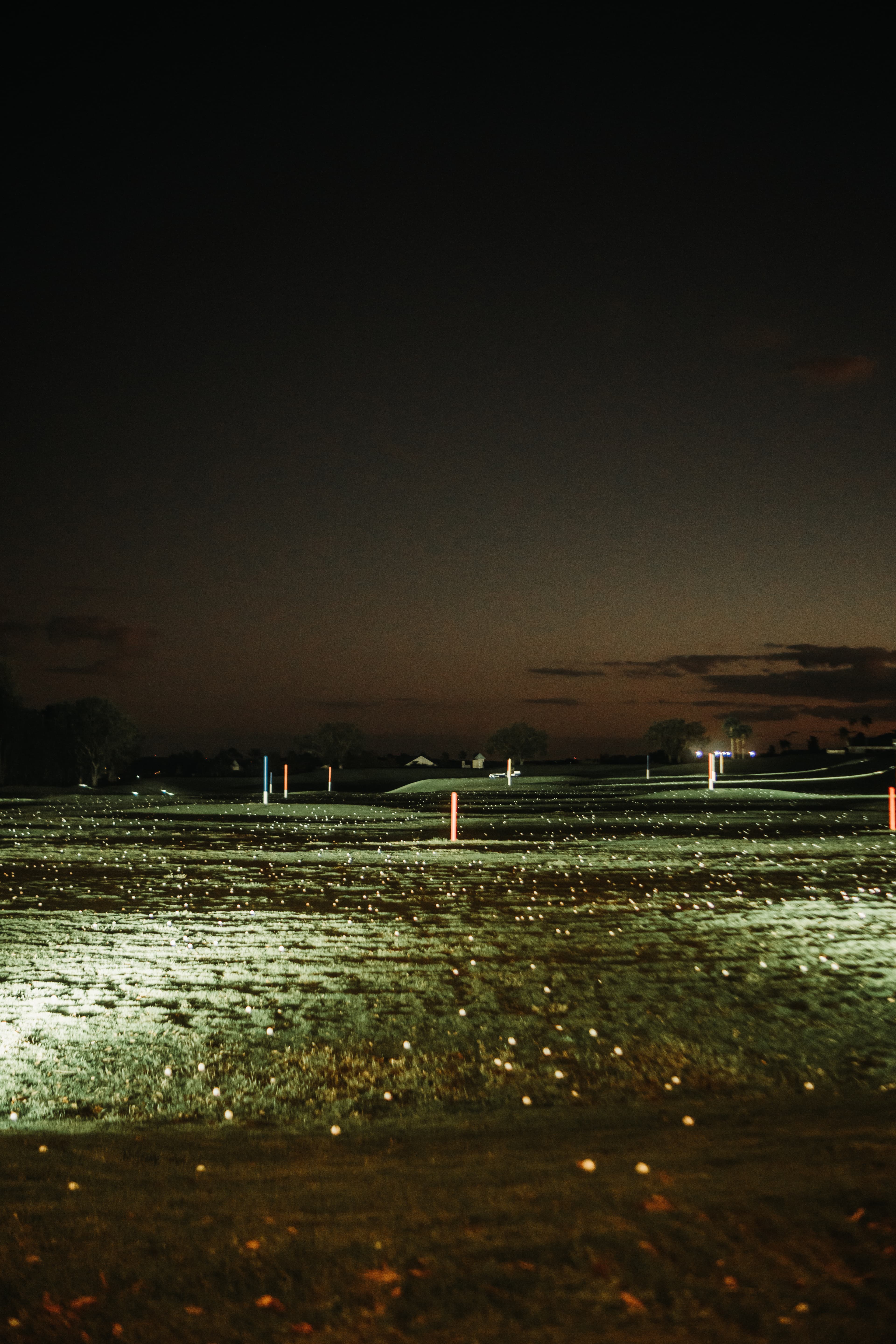 Driving range at night with scattered golf balls and colored target poles